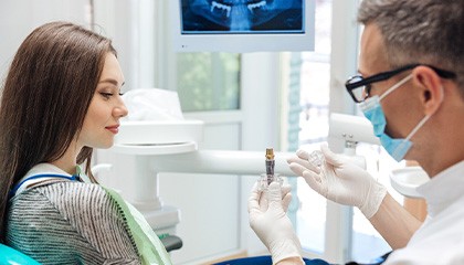 Dentist showing sample dental implant to patient in dental chair