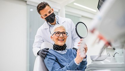 Woman with black glasses smiling at reflection in handheld mirror