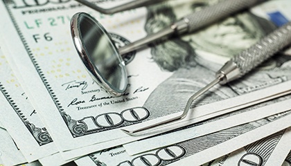 A set of dental tools piled on top of many hundred-dollar bills