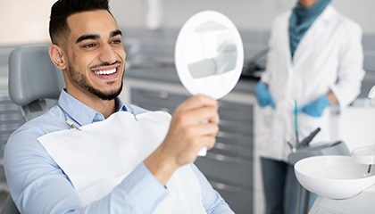 Man smiling while looking at reflection in handheld mirror