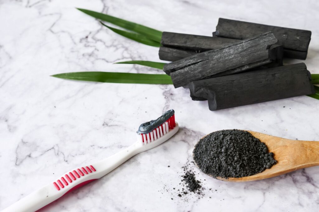 Activated charcoal sticks, spoonful of powder, and toothbrush with black toothpaste on marble surface